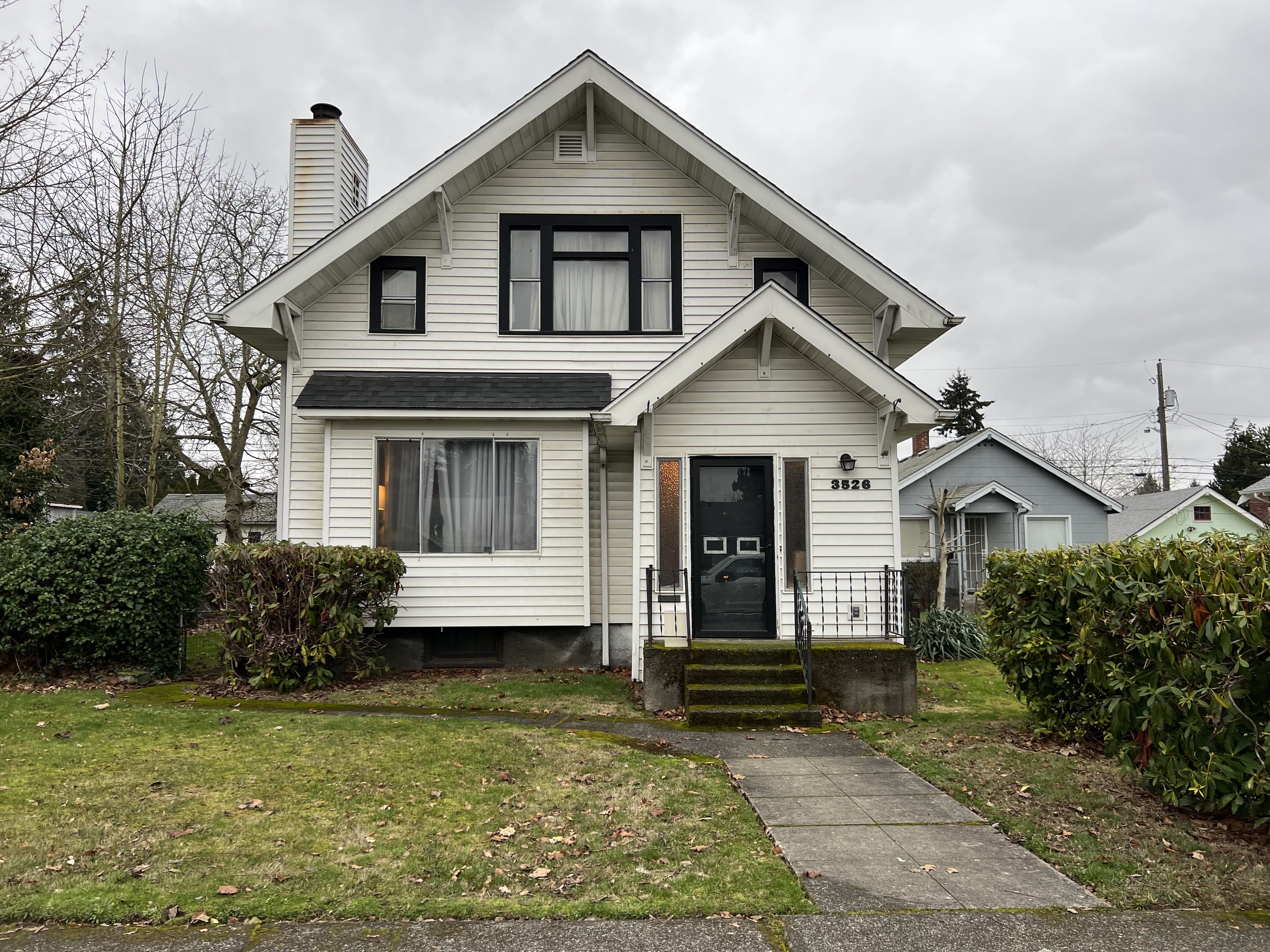 White two-story house with black front door, front lawn, and cloudy sky in a residential neighborhood.