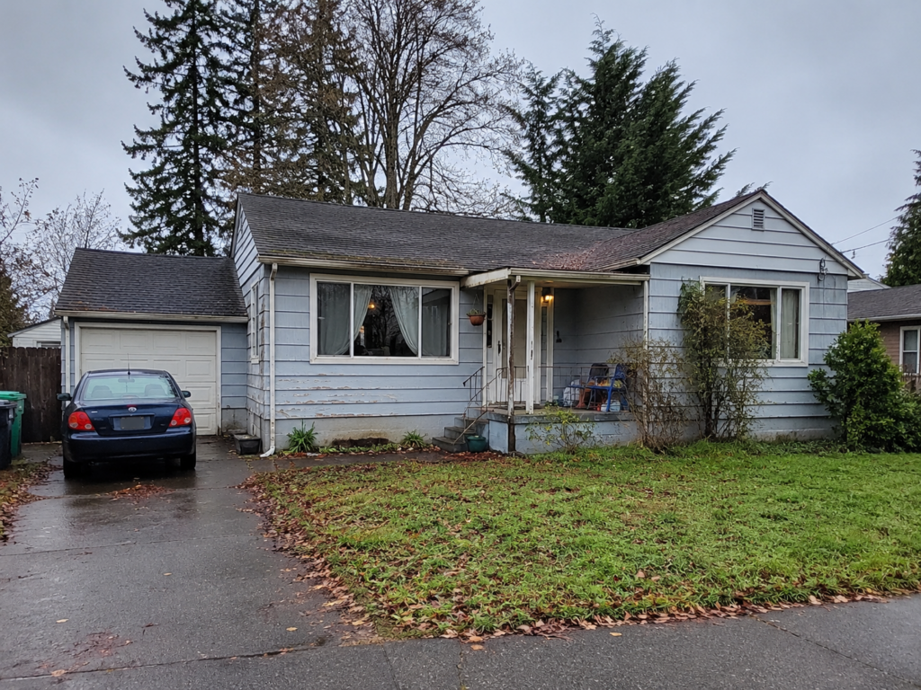 Older tenant occupied house in Olympia, WA, with worn exterior siding, overgrown shrubs, and a wet front yard, representing an as is cash home sale.