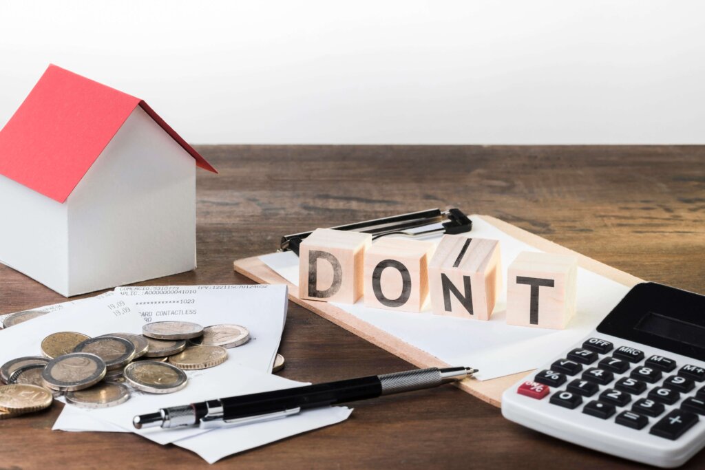 The word DONT on top of a clipboard beside a calculator, a pen, some coins, and a miniature house.