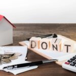 The word DONT on top of a clipboard beside a calculator, a pen, some coins, and a miniature house.