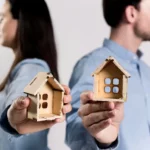 People holding 2 houses made of cardboard