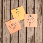 The word idea, question mark, and a light bulb on a post-it note.