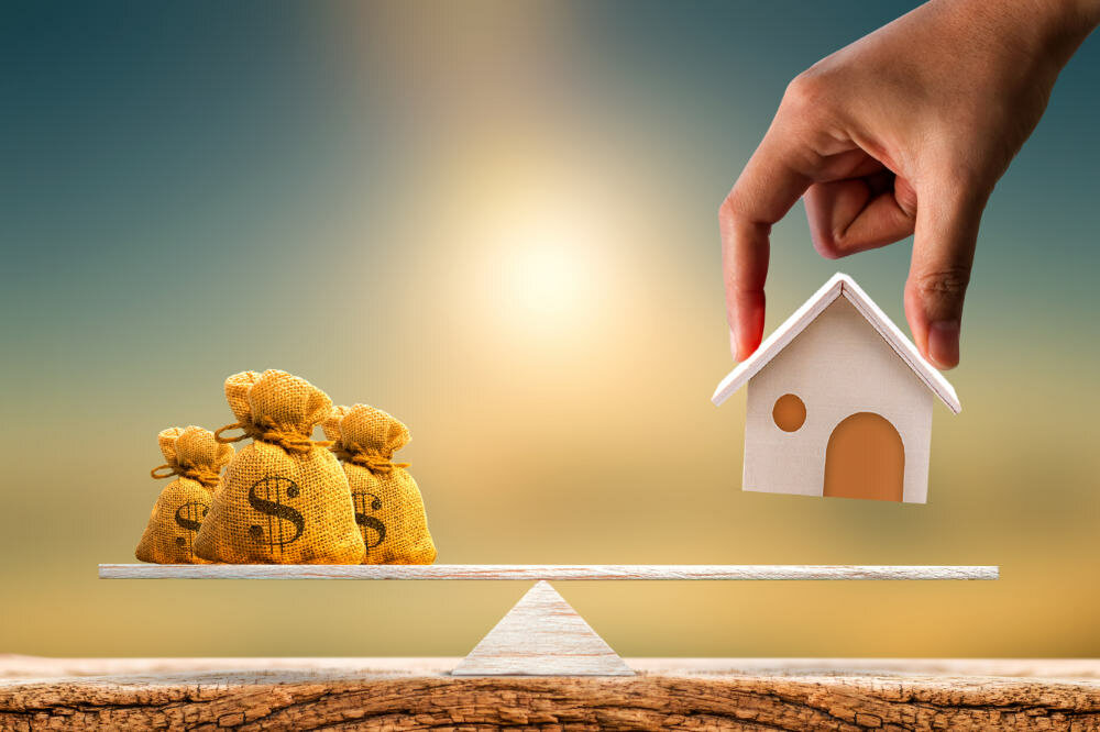 Woman hand hold a wooden home model and money bag put on the scales with balance put on the wood on sunlight, Saving for buy a new house or real estate and loan for plan business investment concept.