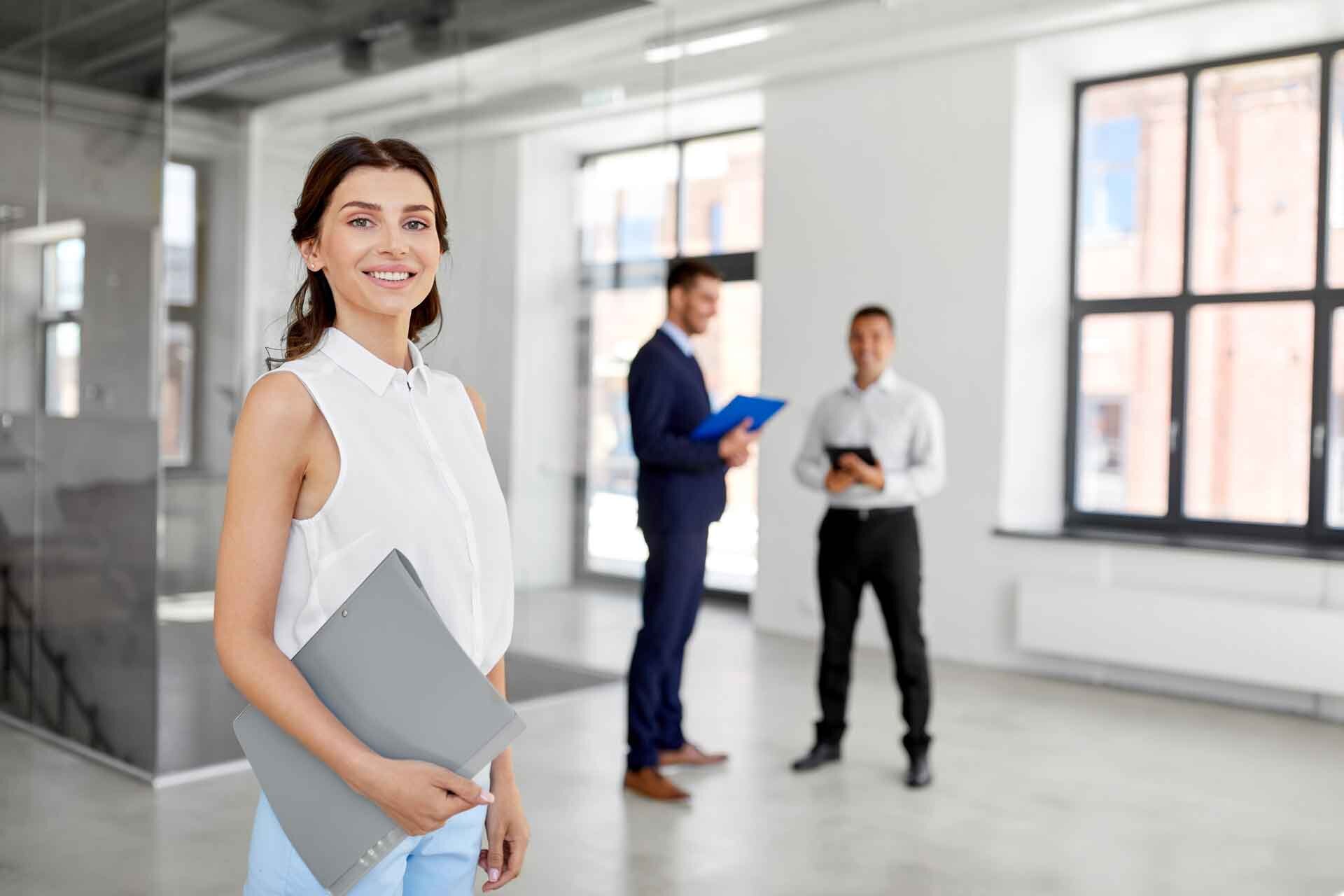 business professional female with two men in the foreground of a loft-industrial office space
