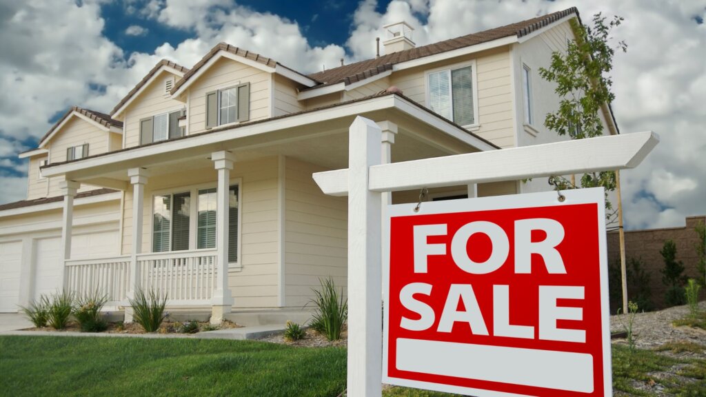 A signboard saying "For Sale" with a white house in the background.
