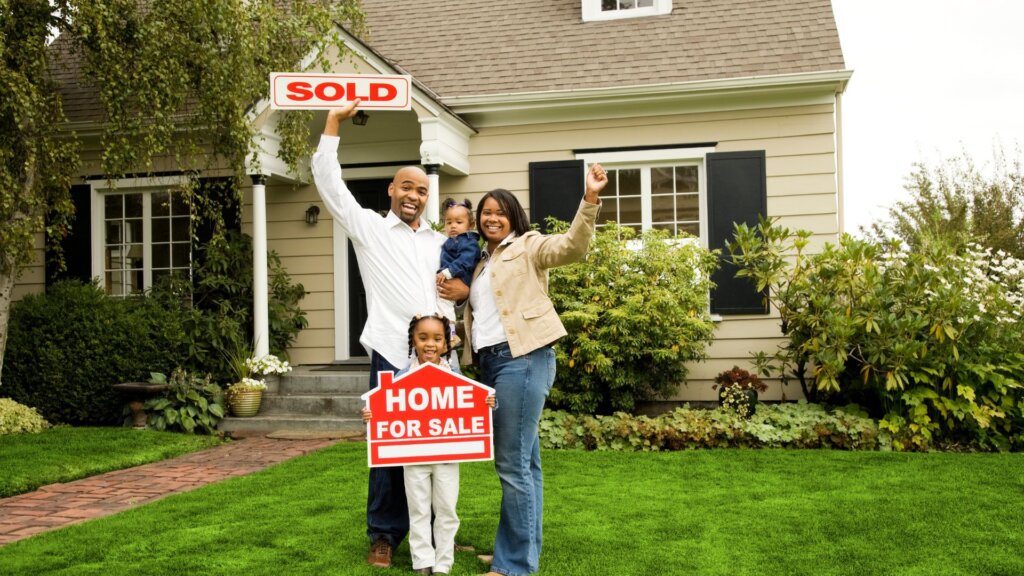 A family holding up a signboard that says "Sold" with a house in the background