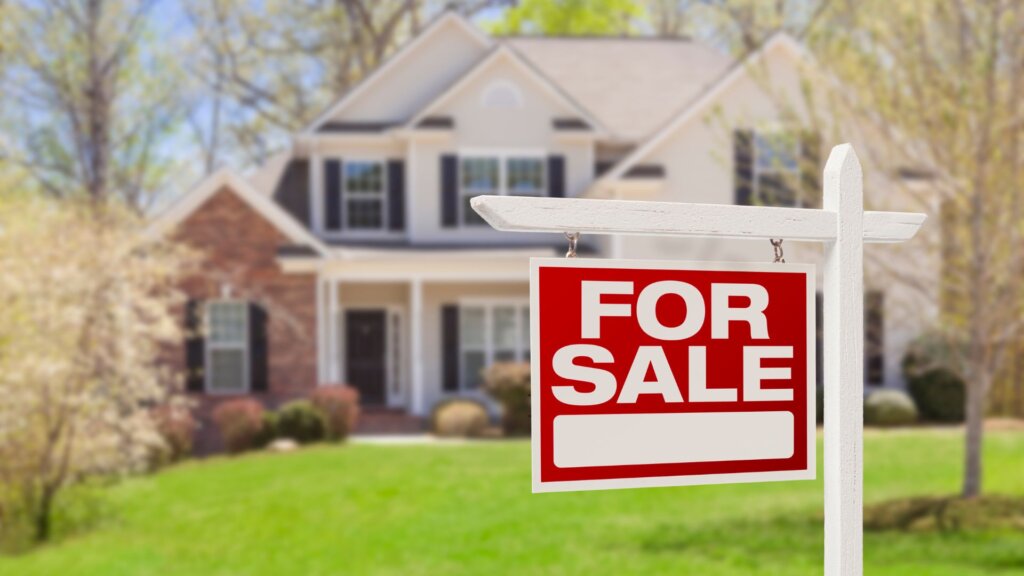 A signboard that says "For Sale" with a house in the background