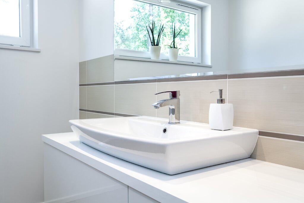 white sink with a stailess faucet and a mirror above it