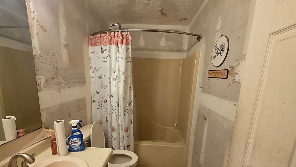 Unfinished bathroom renovation with stripped walls and a damaged ceiling in a Pensacola house we bought as-is