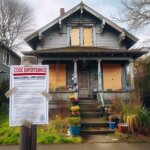 Washington house with peeling paint, boarded windows, and a city notice posted near the front door