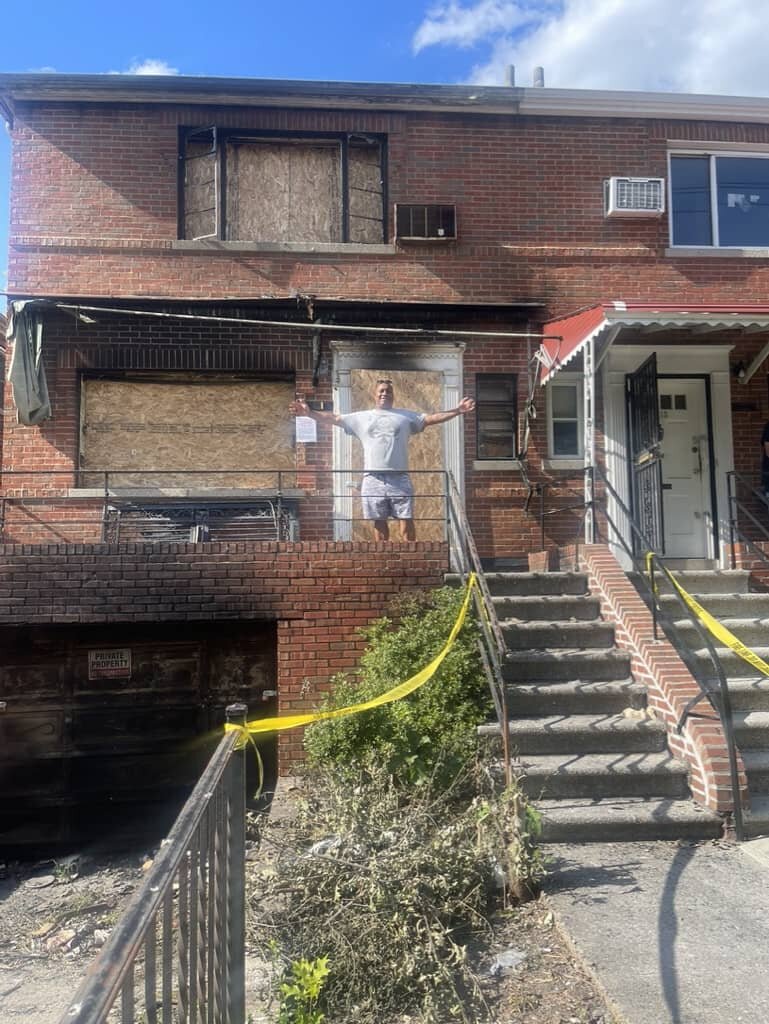 Real estate professional from We Buy Houses NYC standing in front of a fire-damaged property in New York City.