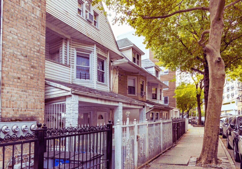 Older wood-frame and brick multi-family homes on a tree-lined Kingsbridge Bronx street — 718Homebuyers buys houses like these fast for cash