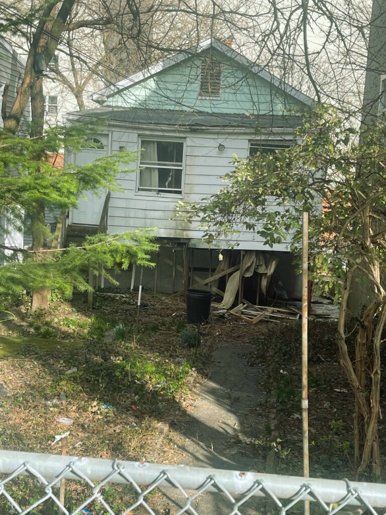 Distressed single-family house in Olinville Bronx NY with structural damage and overgrown yard