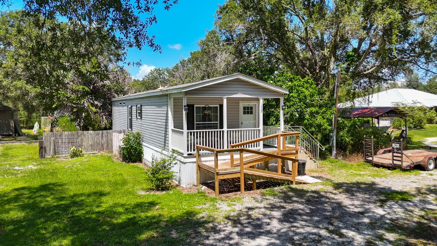 A mobile home listed by Florida Mobile Home Solutions in Arcadia, Florida, with a covered deck and mature trees
