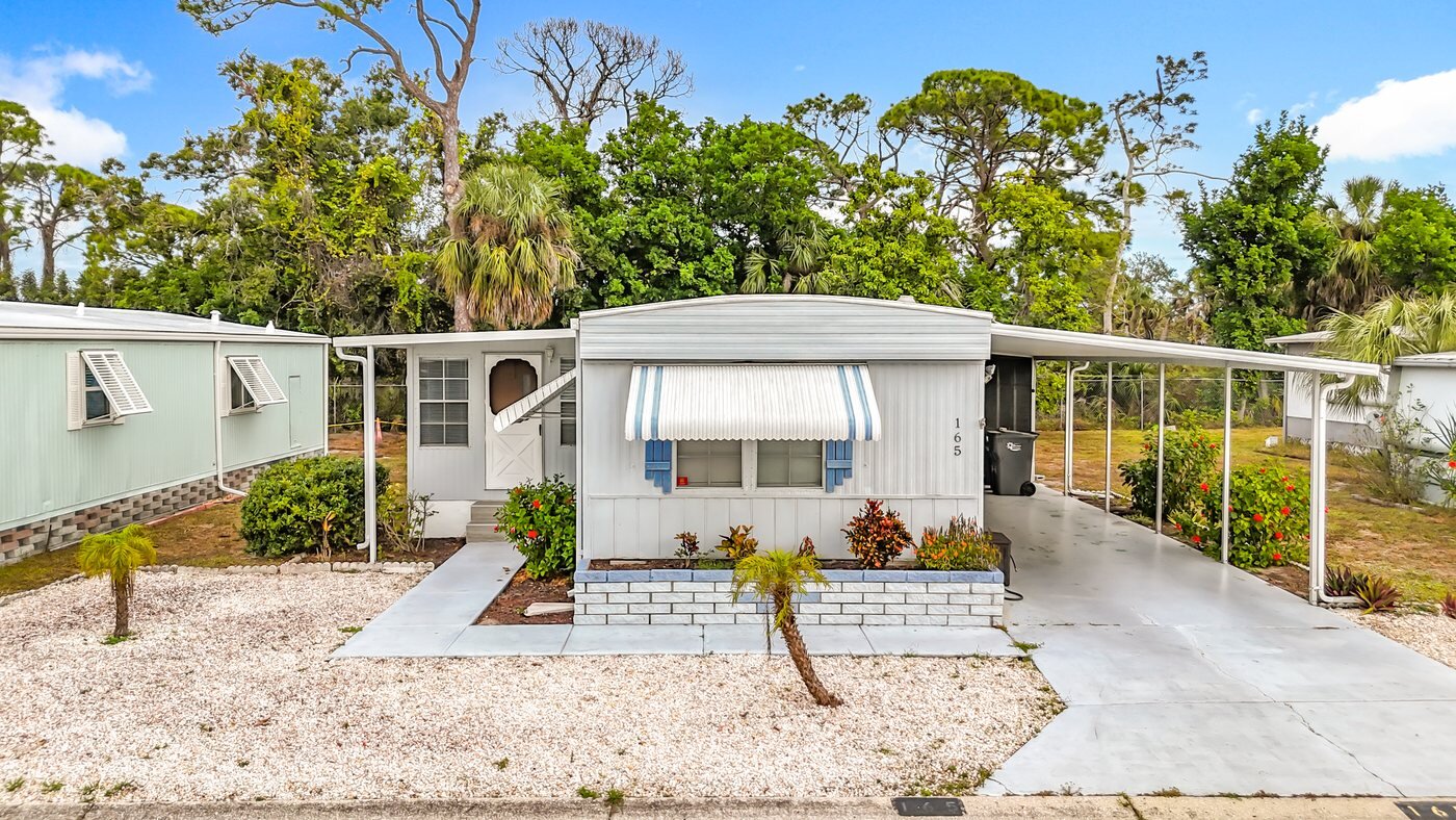A mobile home listed by Florida Mobile Home Solutions in Bradenton, Florida, with a carport, awnings and a paved drive