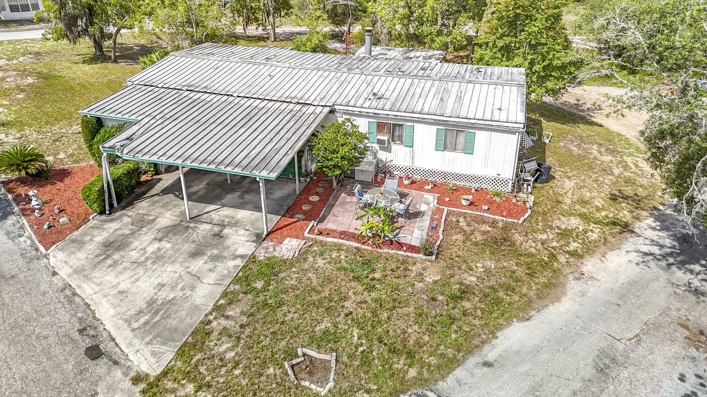 A mobile home listed by Florida Mobile Home Solutions in Brooksville, Florida, with a metal roof and carport on a wooded lot