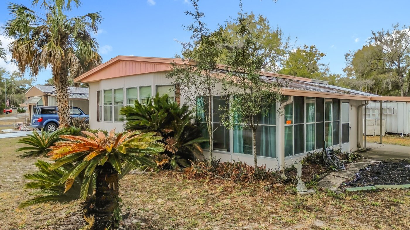 A mobile home listed by Florida Mobile Home Solutions in Crystal River, Florida, with a carport and mature palms