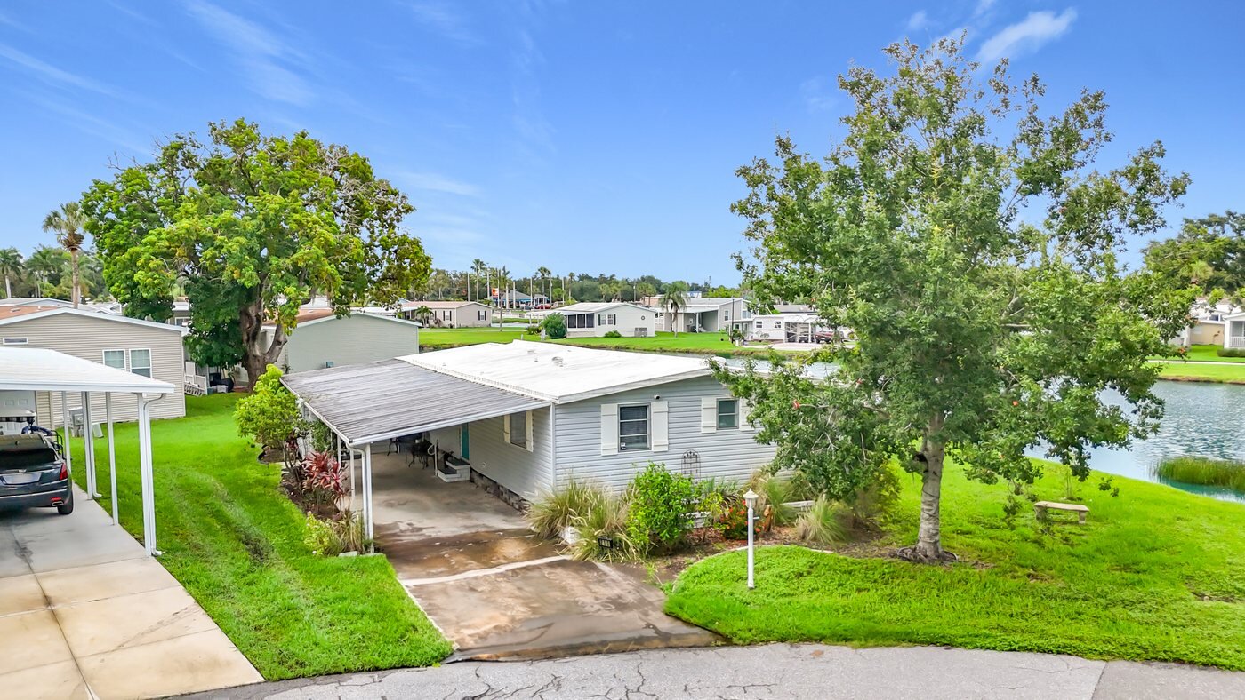 A mobile home listed by Florida Mobile Home Solutions in Ellenton, Florida, beside a lake with mature landscaping