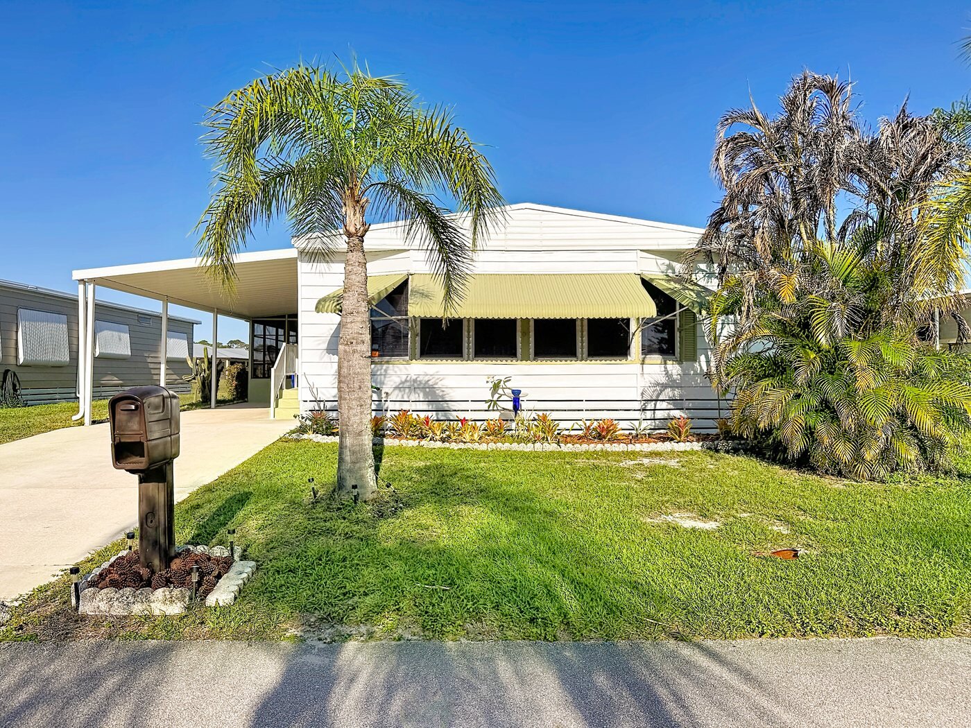 A mobile home listed by Florida Mobile Home Solutions in Fort Pierce, Florida, with a carport and mature palms