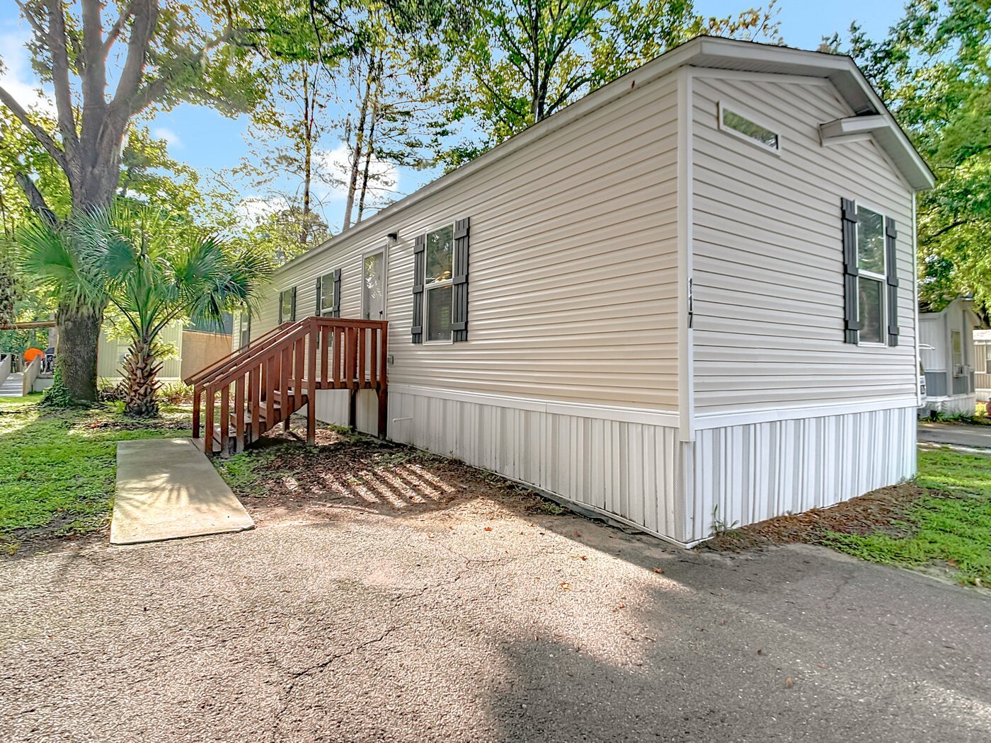 A mobile home listed by Florida Mobile Home Solutions in Gainesville, Florida, with a wooden deck and mature trees