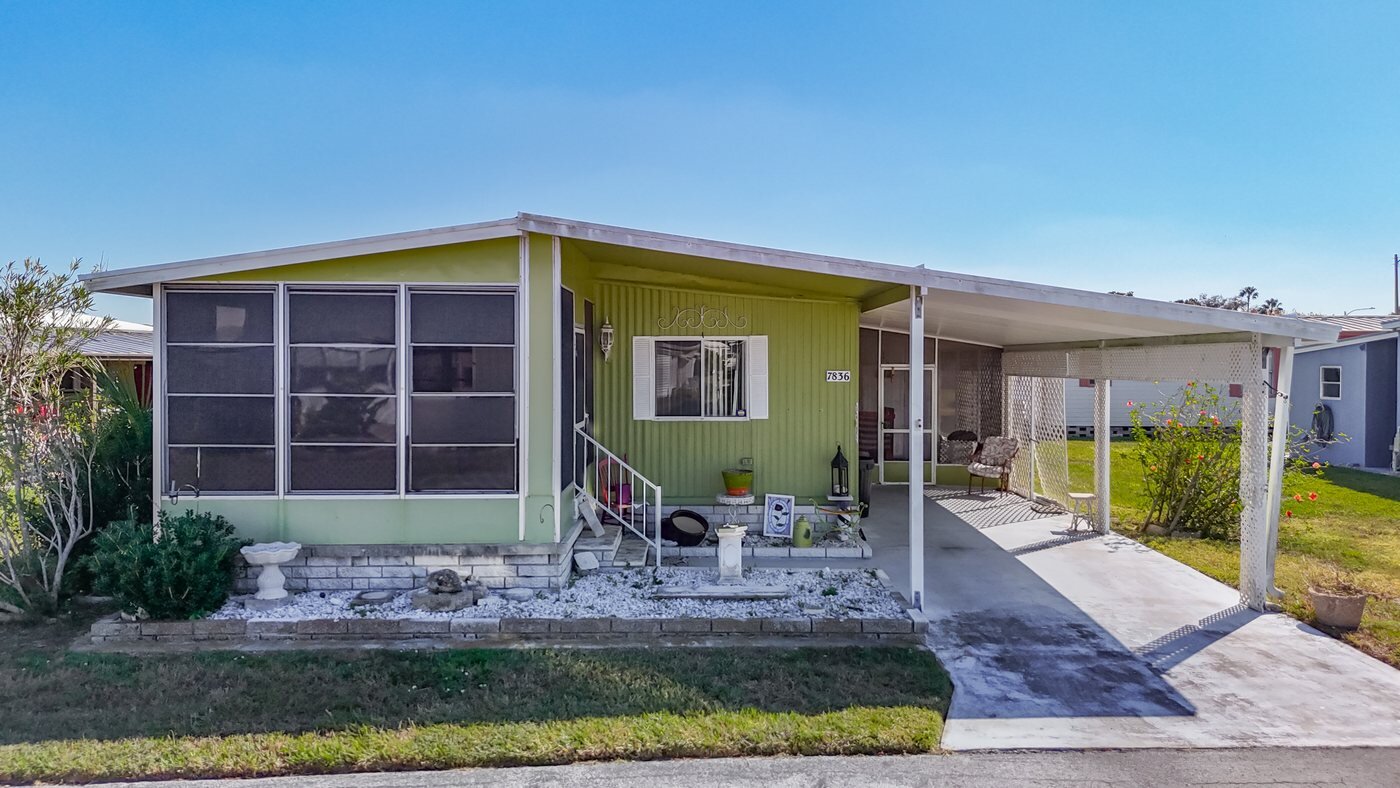 A mobile home listed by Florida Mobile Home Solutions in Hudson, Florida, with a screened porch and covered carport