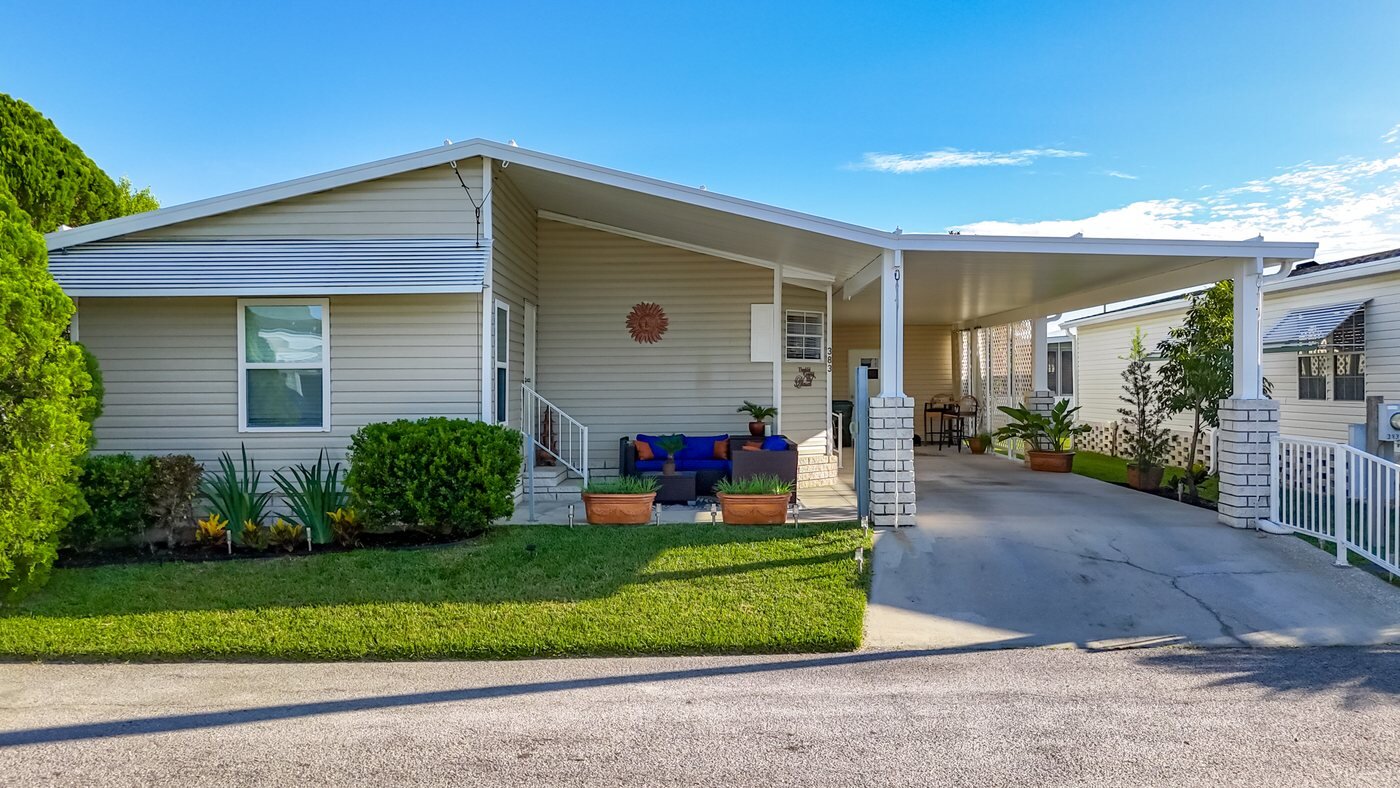 A mobile home listed by Florida Mobile Home Solutions in Lakeland, Florida, with a carport and landscaped front yard