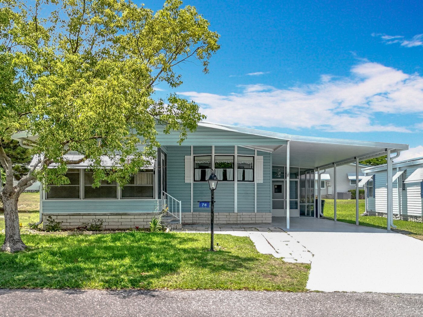 A mobile home listed by Florida Mobile Home Solutions in Leesburg, Florida, with a carport and mature shade trees