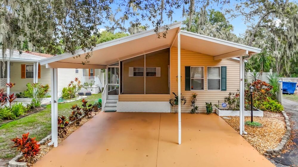 Florida mobile home with covered carport, screened porch and landscaped beds, professionally photographed for a Florida Mobile Home Solutions listing