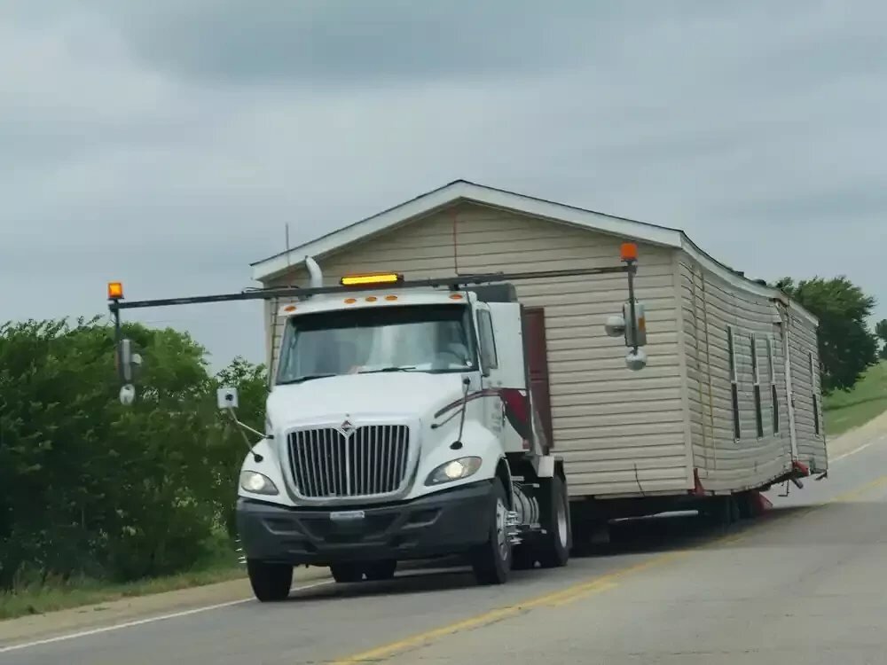 A used mobile home being transported by truck on a highway to its new location