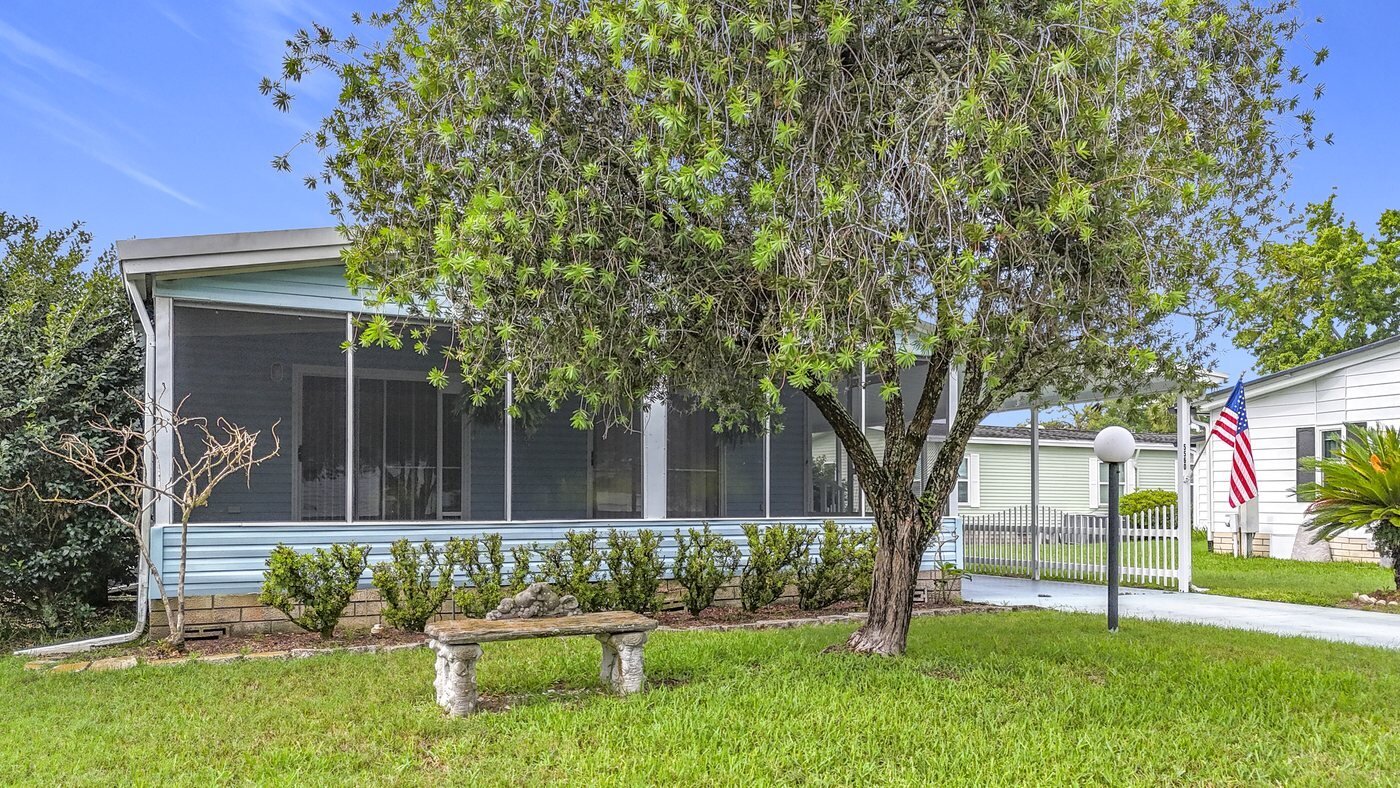 A mobile home listed by Florida Mobile Home Solutions in Ocala, Florida, with a screened porch and mature shade trees