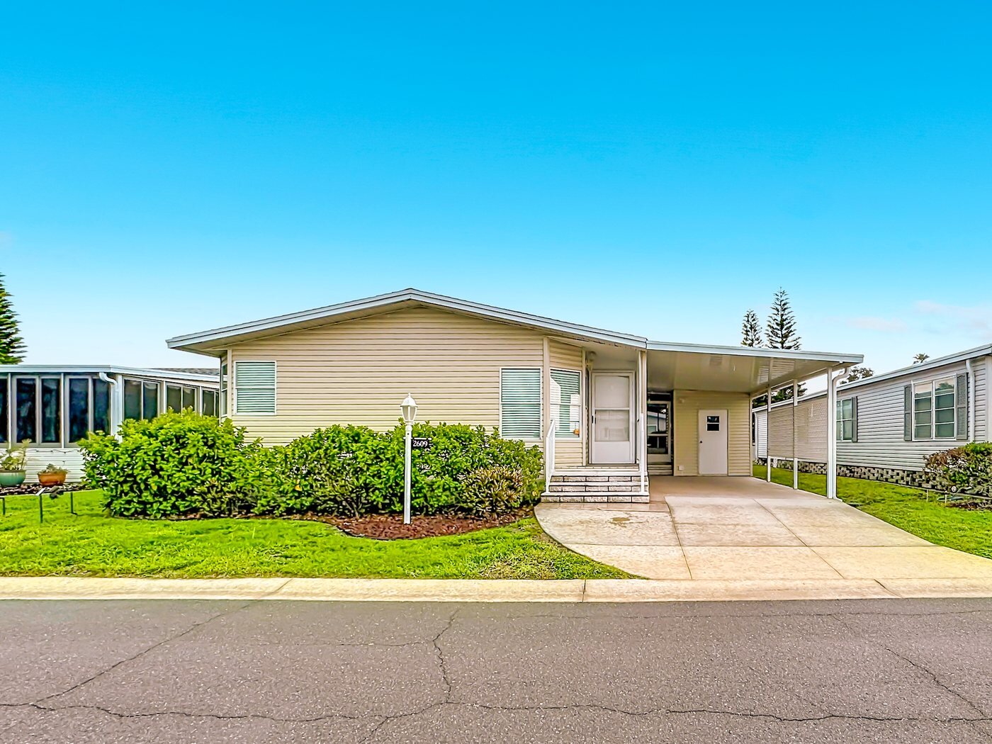 A mobile home listed by Florida Mobile Home Solutions in Palmetto, Florida, with a carport and landscaped frontage