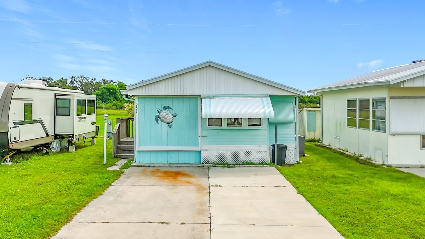 A mobile home listed by Florida Mobile Home Solutions in Ruskin, Florida, with a carport and mature landscaping