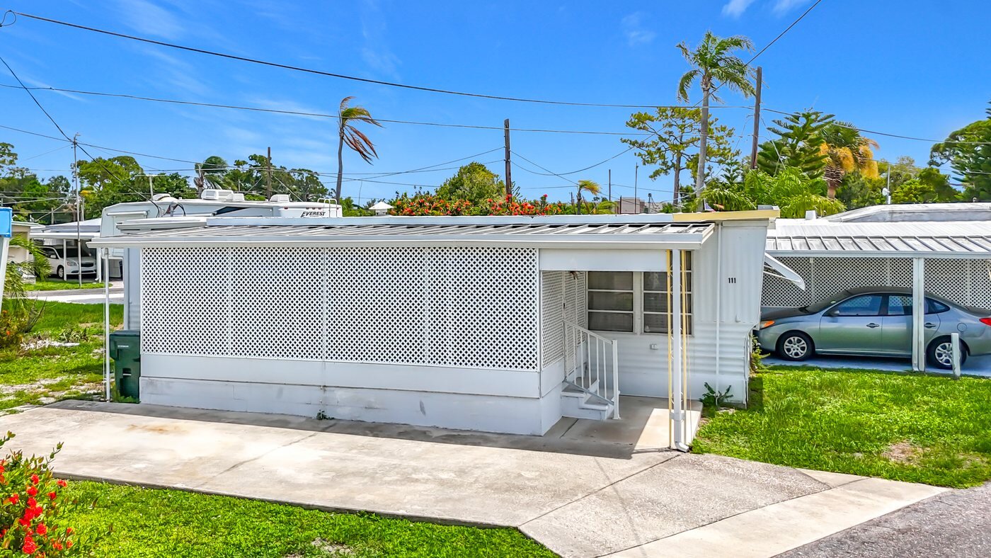A mobile home listed by Florida Mobile Home Solutions in Sarasota, Florida, with a carport, awnings and a paved drive
