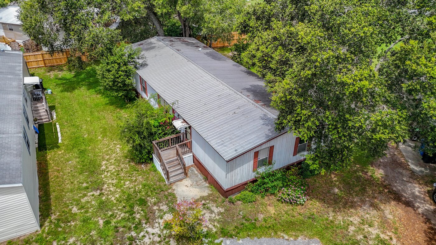 A mobile home listed by Florida Mobile Home Solutions in Tampa, Florida, viewed from above with a metal roof and mature trees