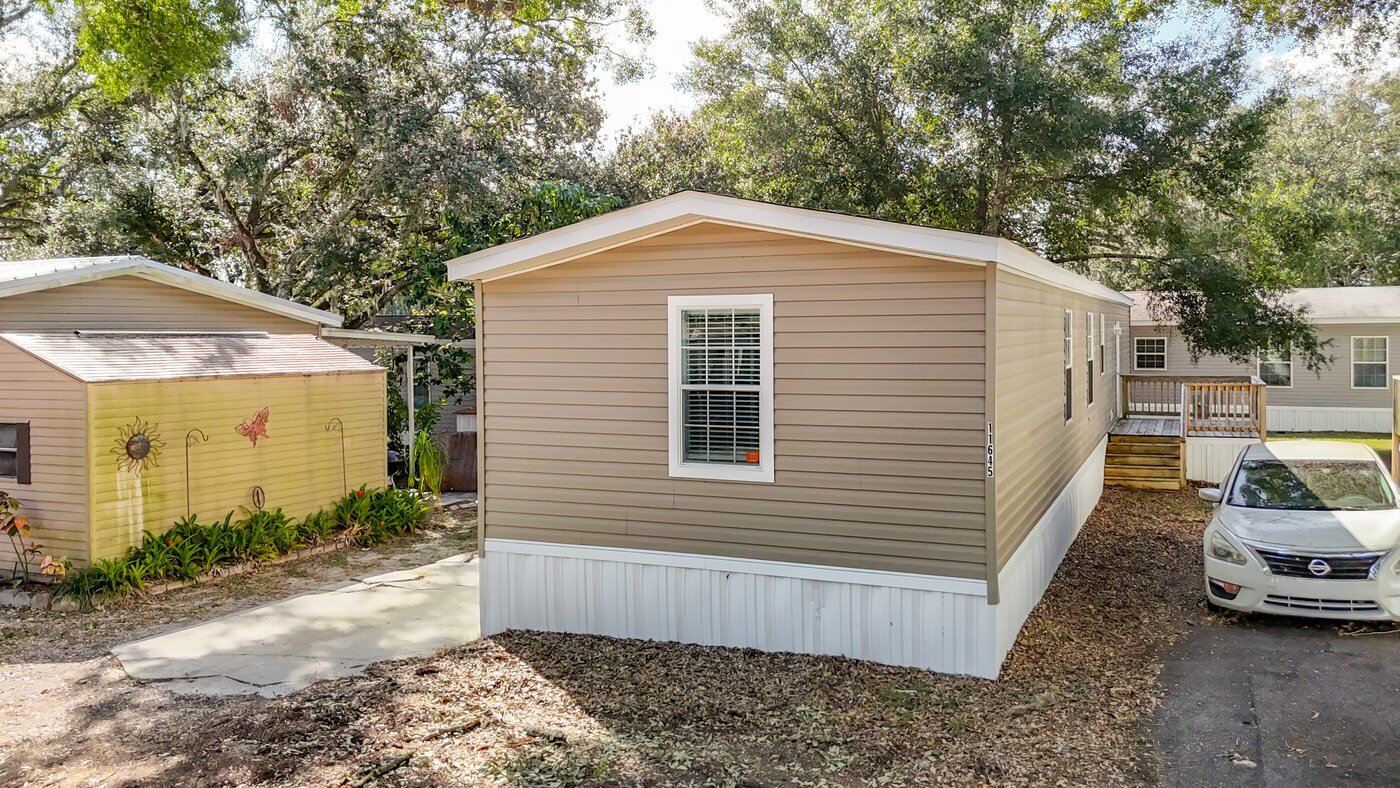 Aerial view of a mobile home in a Thonotosassa, Florida community with a carport and mature oaks