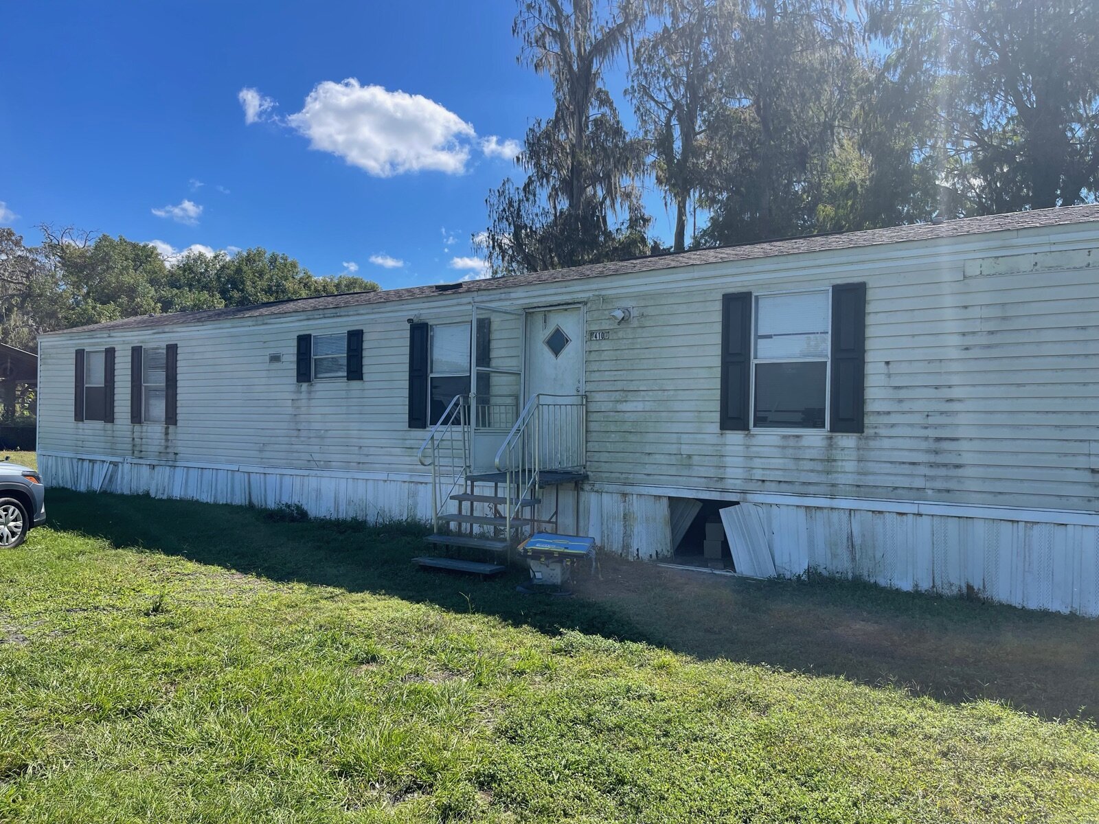 A weathered single wide mobile home in Florida with mildewed siding and worn skirting, structurally sound and sellable
