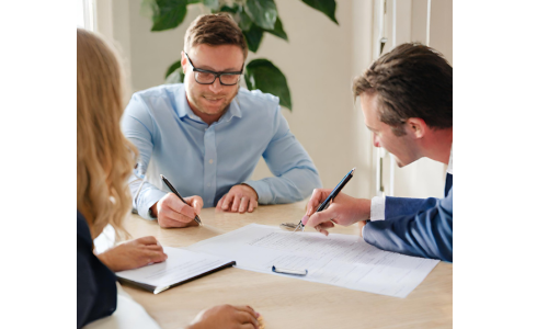 A photo of a homeowner signing a sales contract with a buyer and representative from a cash home buyer.