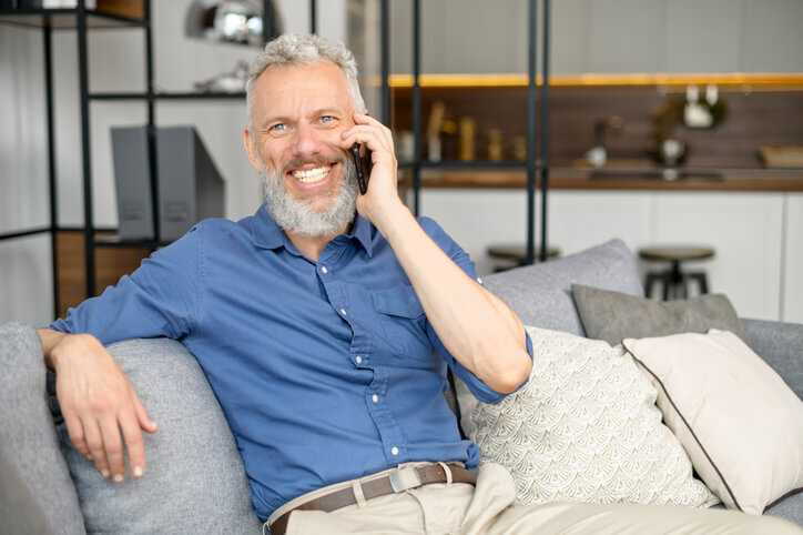 Senior-bearded-guy-sitting-down-on-the-comfortable-couch-and-talking-on-the-smartphone-sell-your-house-fast-golocalinvestor.com