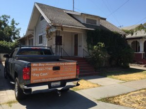 Photo of truck with "We Buy Houses In Any Condition" sign in front of a rundown house in Stockton, California.