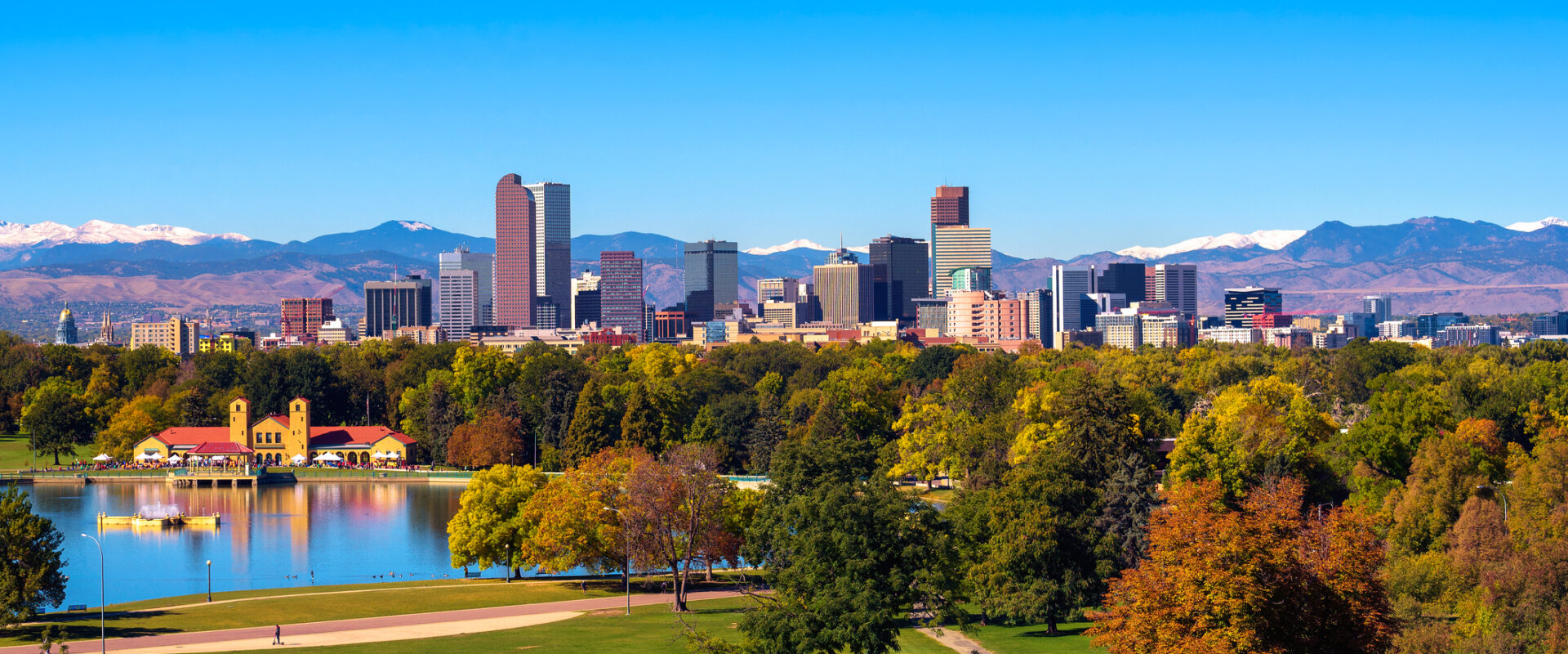 City skyline of Denver Colorado downtown with snowy Rocky Mountains and the City Park Lake.