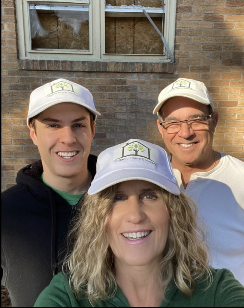 Photo of Cynthia, Steve & Anthony wearing company logo hats, standing in front of a distressed property.