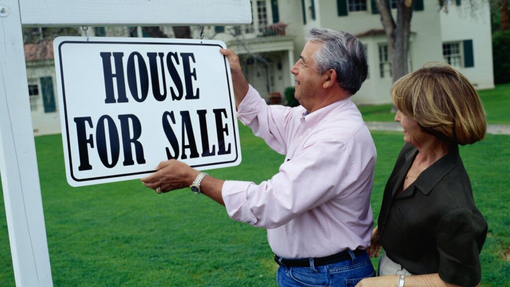 A couple holding a "House for Sale" signboard