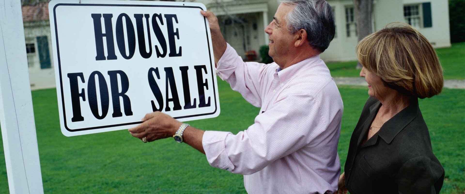 A couple holding a "House for Sale" signboard