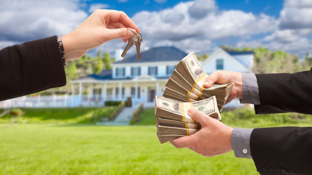 Two pair of hands with one handing over a key and the other a cash