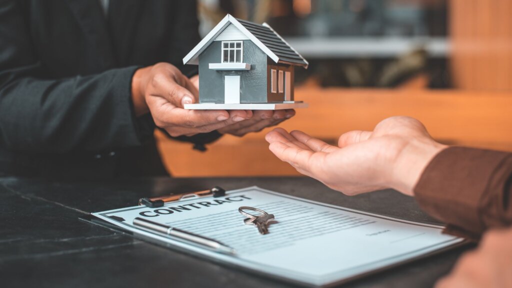 Two pair of hands, with one handing a miniature house model to the other