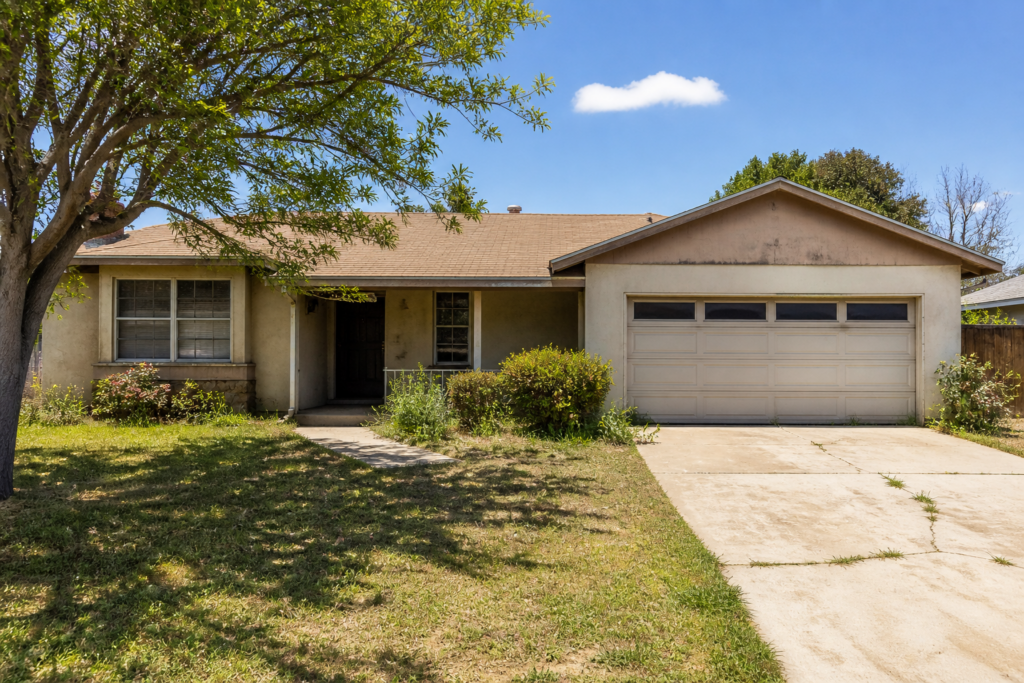 California ranch-style home with deferred maintenance including faded stucco, aging roof, overgrown landscaping, and cracked driveway — the type of as-is property cash home buyers in California purchase without requiring repairs.
