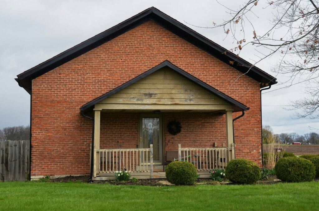 Older brick house with a covered front porch and a wooden fence