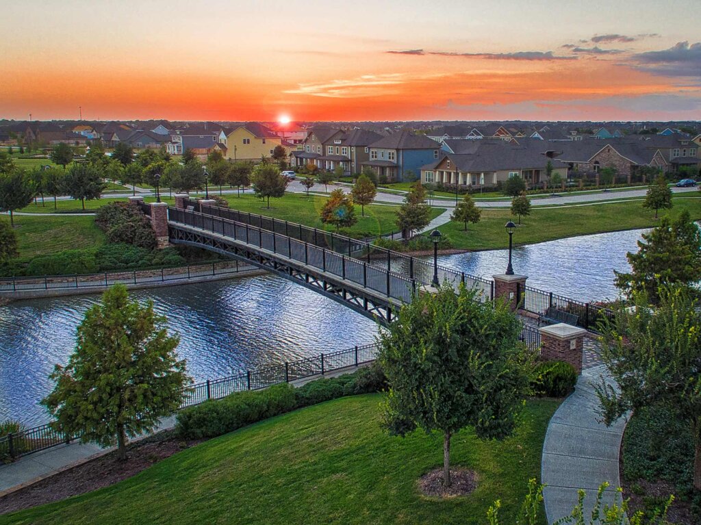 Beautiful sunset in Cypress Texas, image shot from a drone that sees a walking bridge over a lake in Bridgeland, Texas. Many houses on the other side of the bridge.