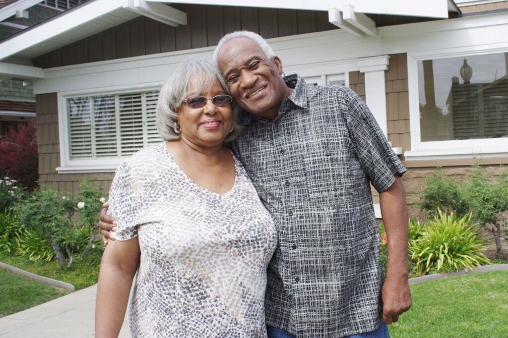 Happy couple standing in front of a house they sold. They had inherited the property and didn't want to deal with repairs and taxes so they sold it to a cash buyer.