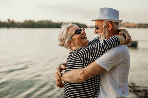 Happy couple laughing beside a lake in Cypress, Texas. They recently sold a house they inherited and are excited to spend some of the money they earned on a trip.
